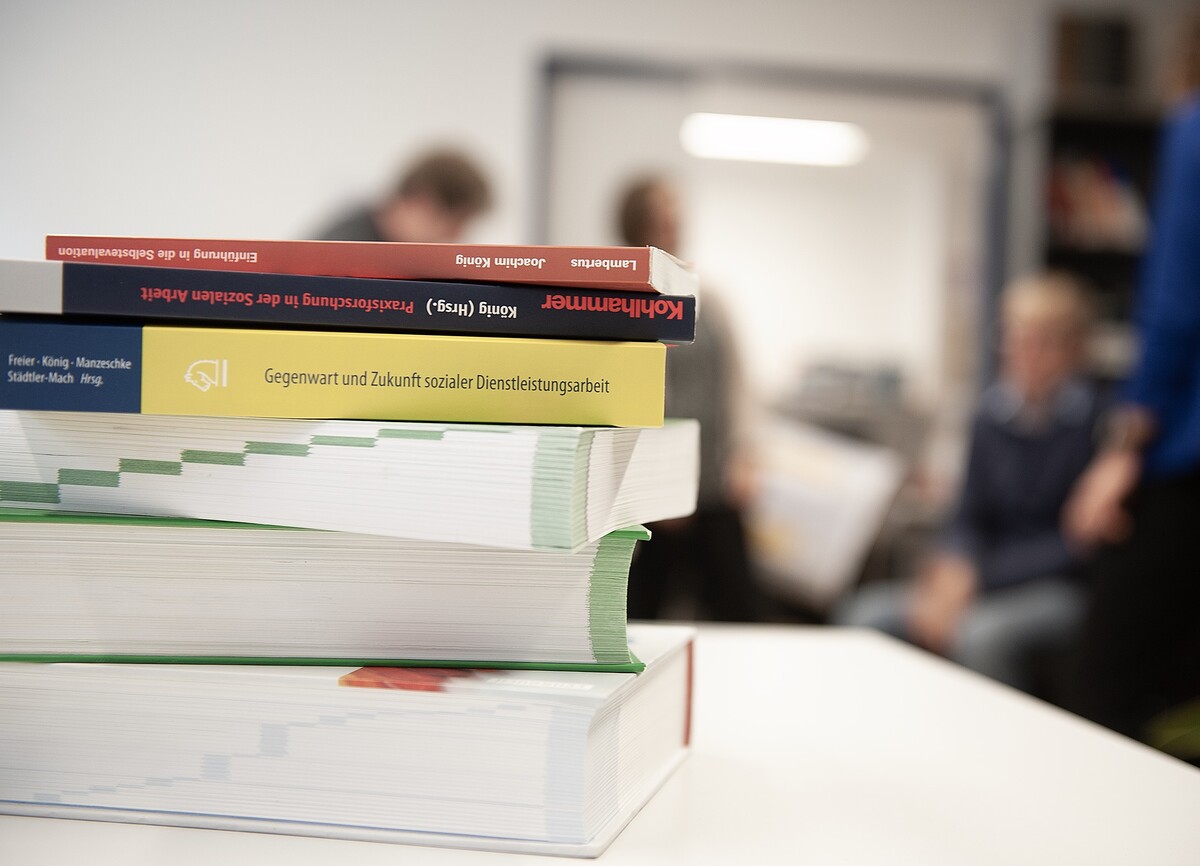 Ein Stapel wissenschaftlicher Bücher vor einer Gruppe von Personen