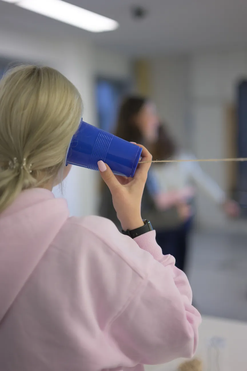 Eine junge Frau hält sich einen Plastikbecher mit befestigter Schnur ans Ohr