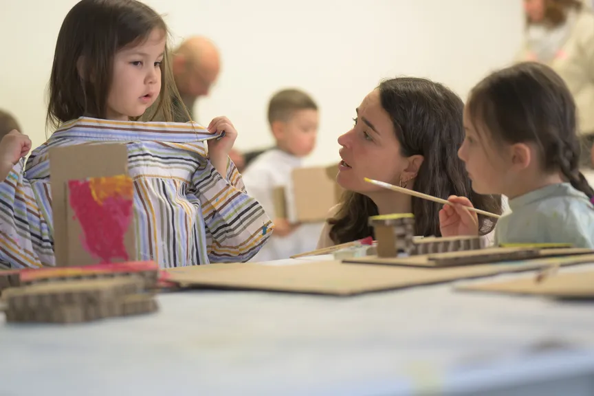 Eine Praxisanleiterin spricht mit Kindern, die etwas bemalen