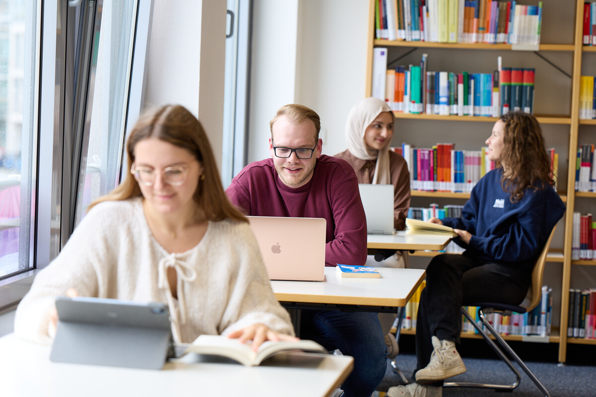 Einige Studierende sitzen an Arbeitsplätzen in einer Bibliothek und arbeiten