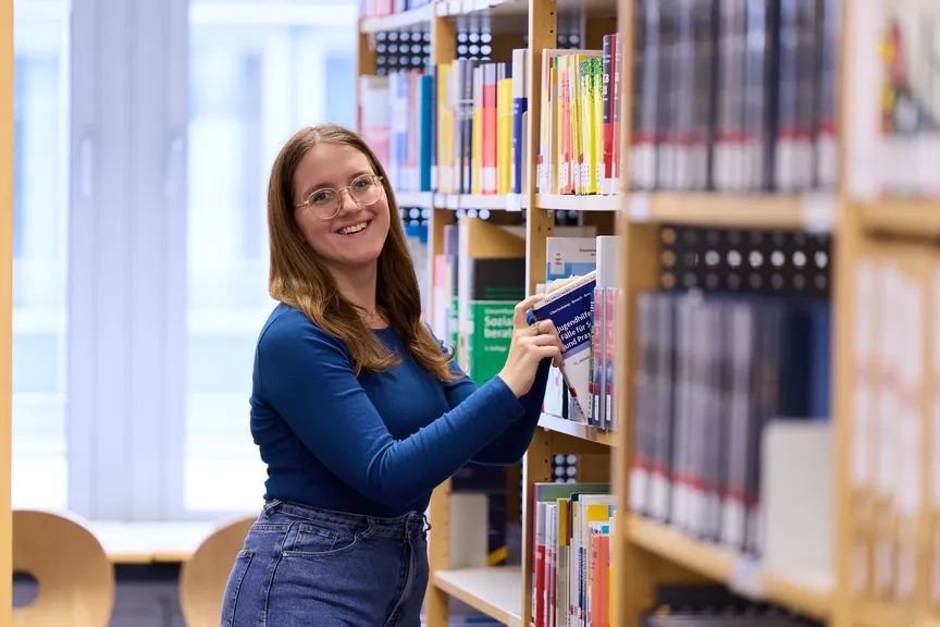 Eine Studierende zieht ein Buch aus einem Regal in einer Bibliothek
