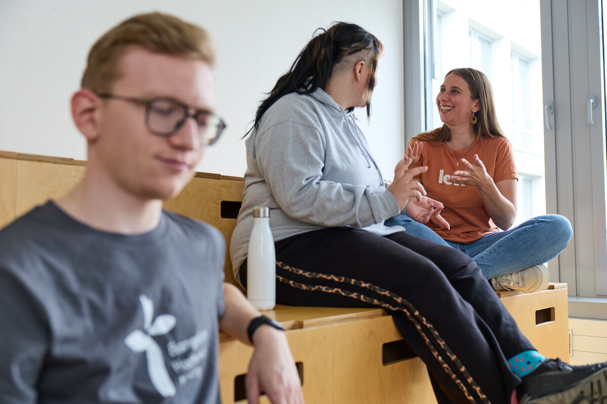 Einige Studierende sitzen auf einer hölzernen Sitzgelegeneheit und unterhalten sich