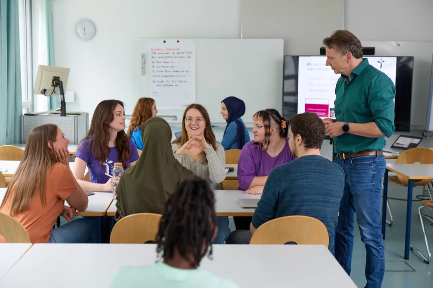 Eine Gruppe Studierender arbeitet miteinander in einem Seminar und unterhält sich mit einem Dozenten