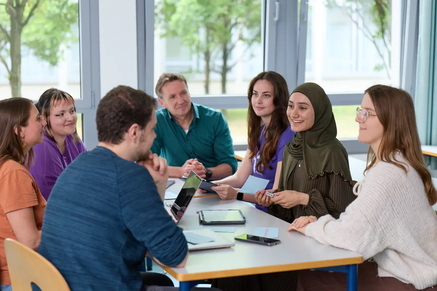 Eine Gruppe Studierender arbeitet miteinander in einem Seminar und unterhält sich mit einem Dozenten