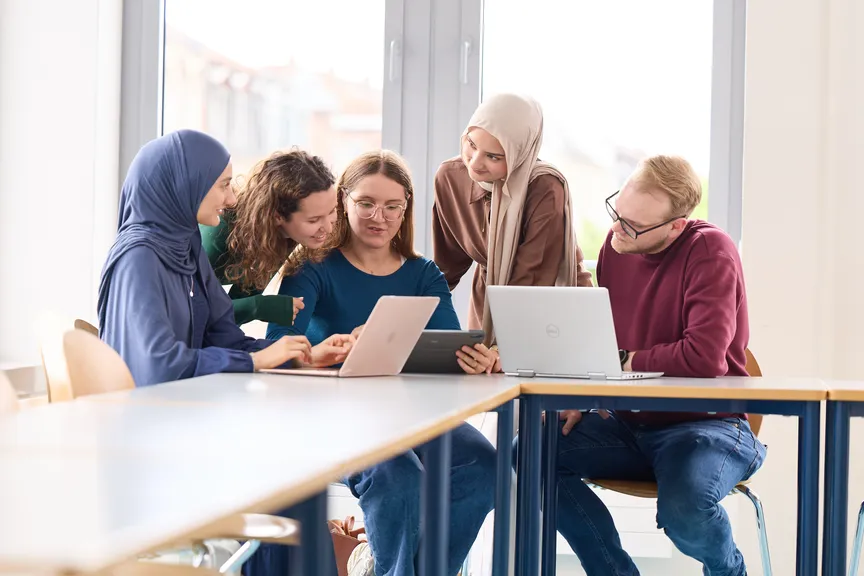 Eine Gruppe Studierender arbeitet an Laptops und diskutiert