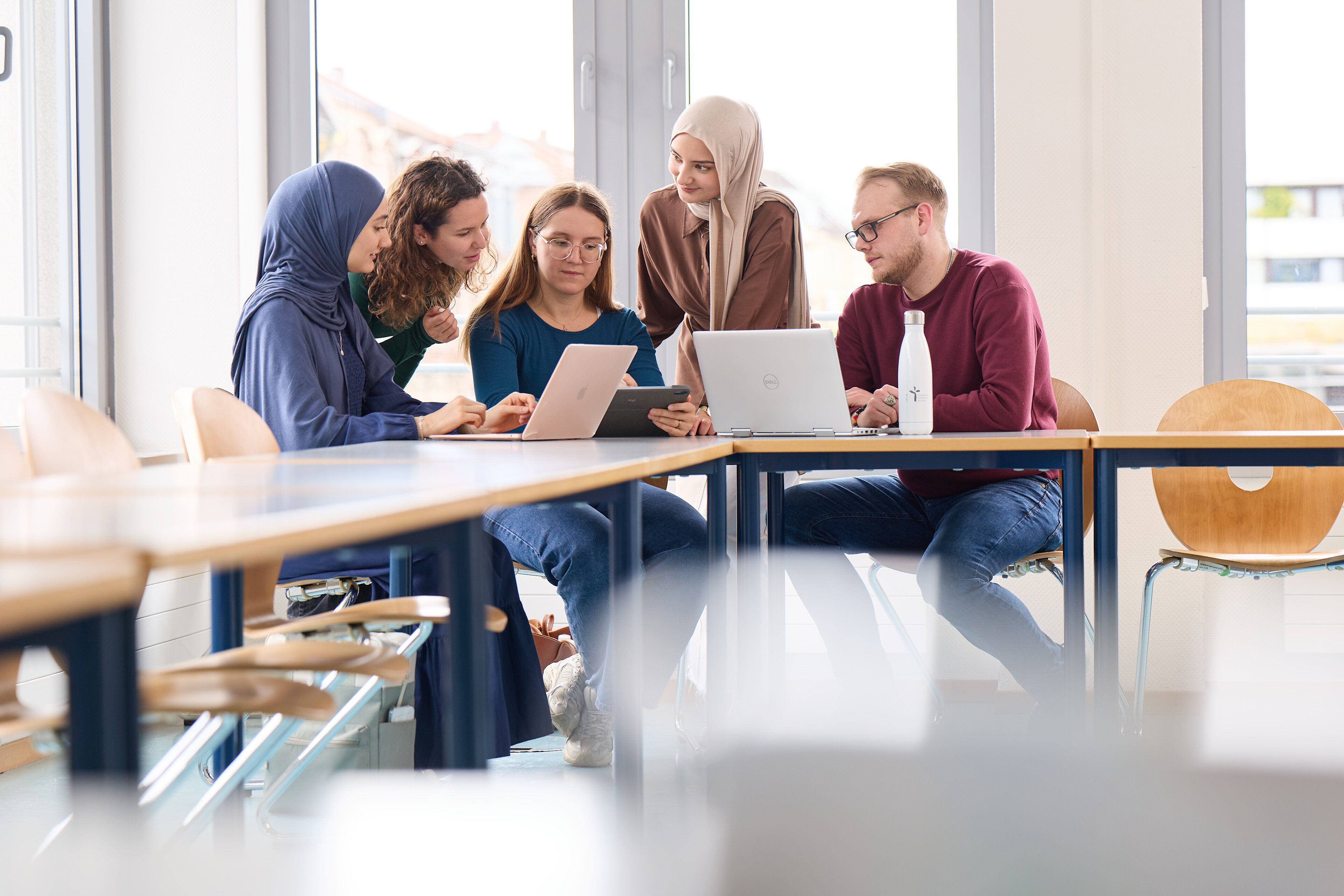 Eine Gruppe Studierender arbeitet an Laptops und diskutiert