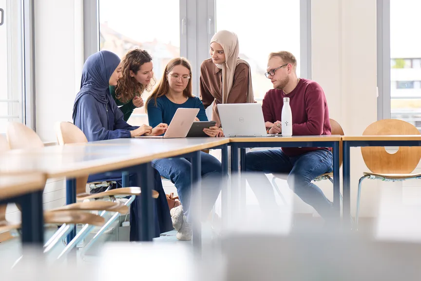 Eine Gruppe Studierender arbeitet an Laptops und diskutiert