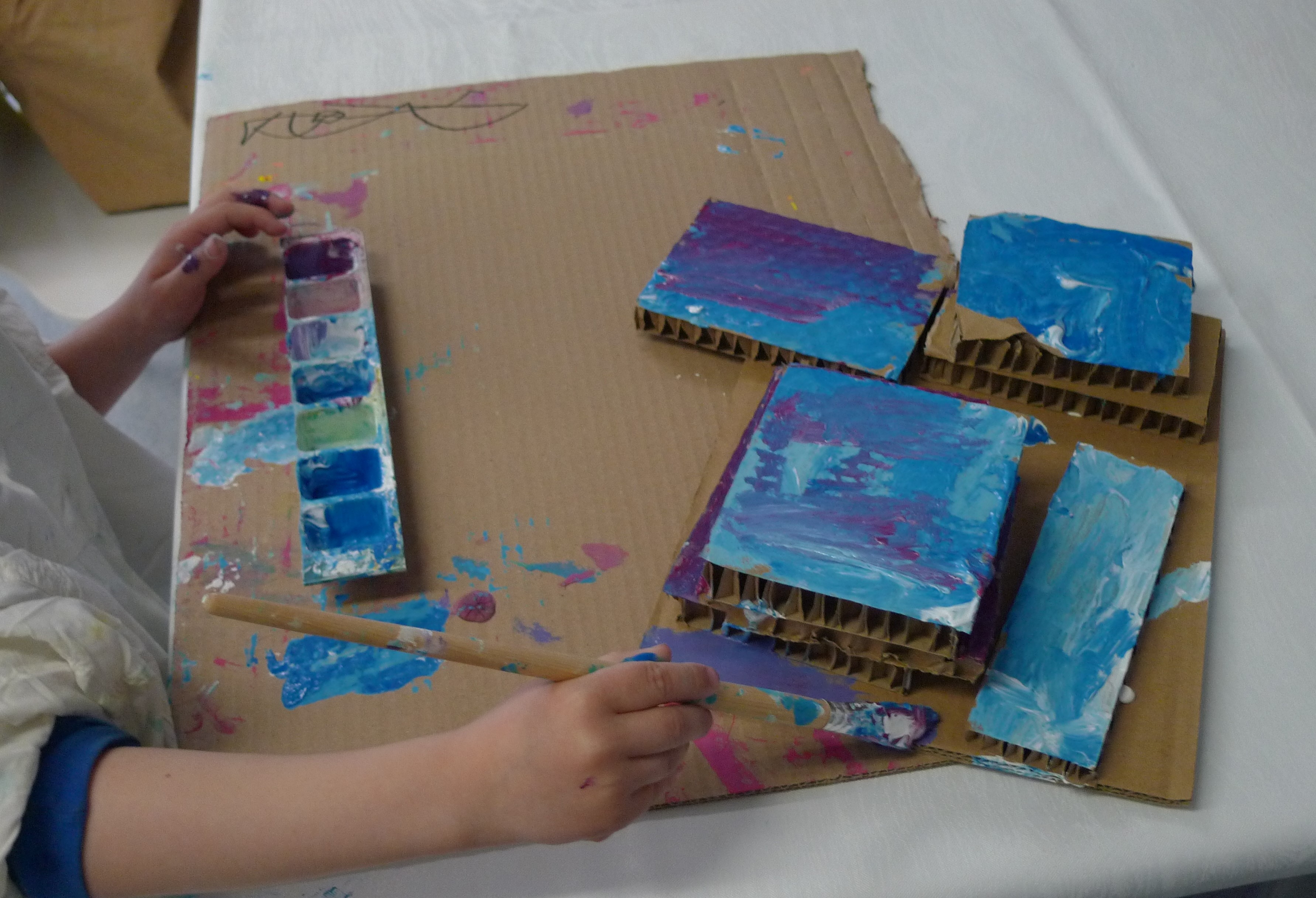 Kinderhand mit Pinsel, malt blaue Flächen auf Pappe