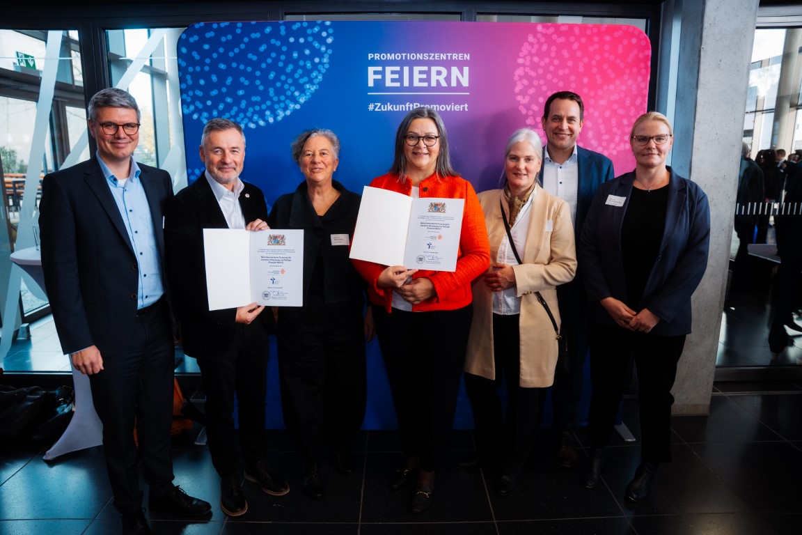 7 Personen, 2 halten eine Urkunde in den Händen