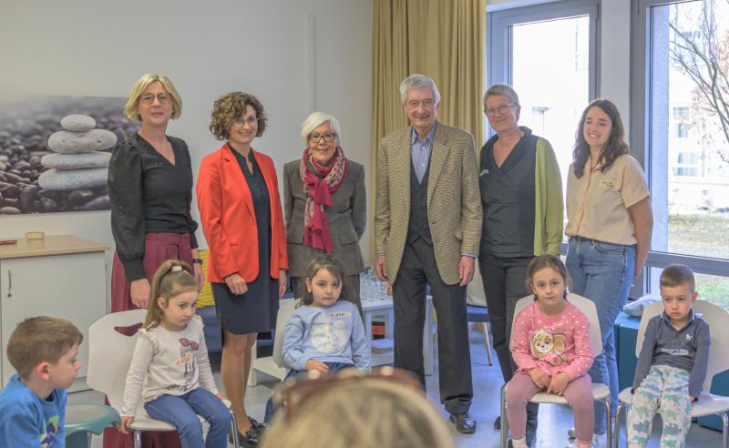 sechst erwachsene Personen, darunter ein Mann, stehen in einer Reihe; davor sitzen Kinder auf Stühlen