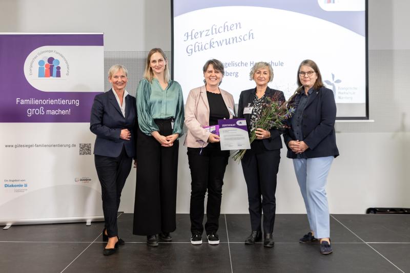 Fünf Frauen stehen in einer Reihe, davon mit Blumen, eine mit einer Urkunde